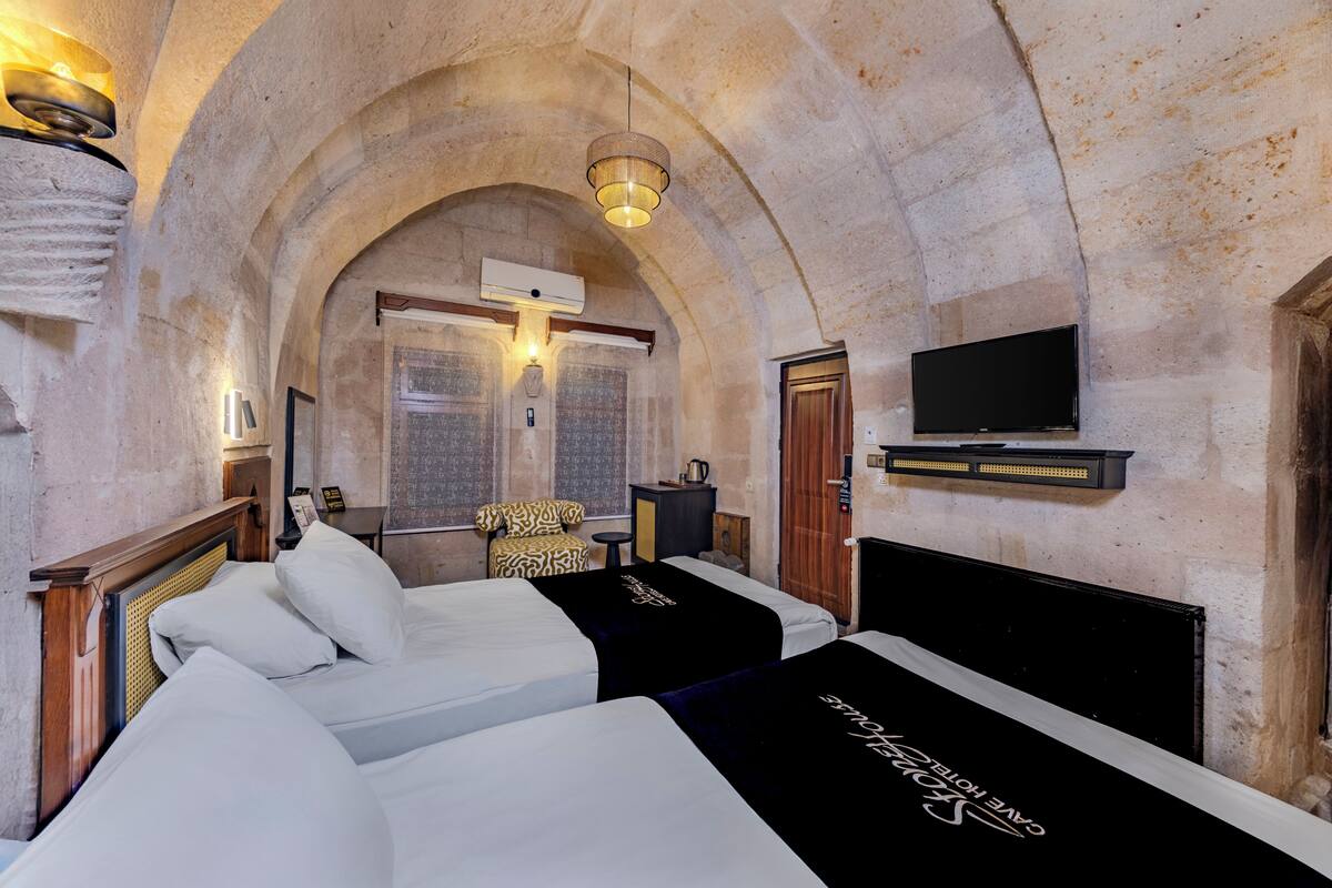 Ein Zimmer mit zwei Betten, Fernseher, gewölbter Decke und Steinwand.