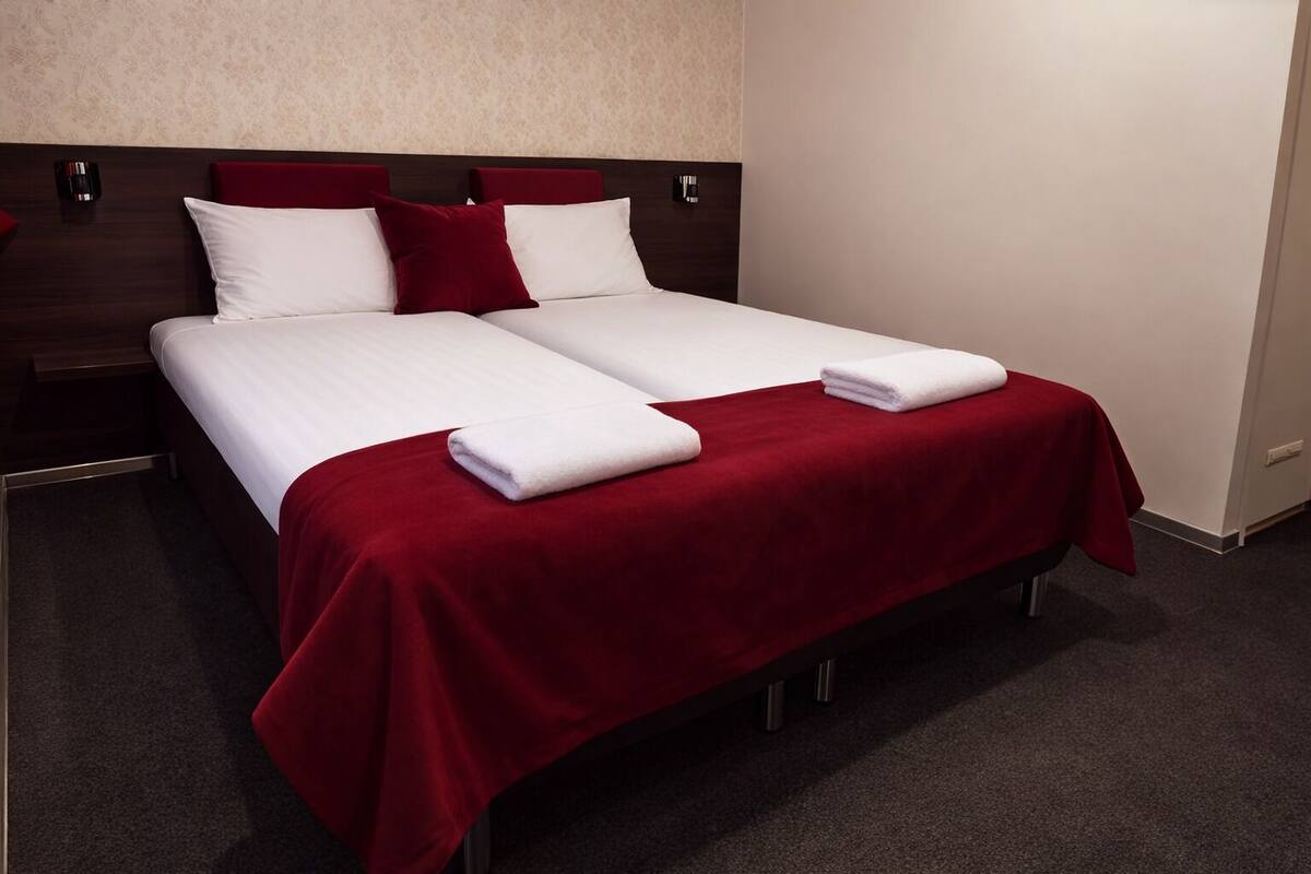Un lit double avec une literie blanche et rouge, deux oreillers et deux serviettes pliées.