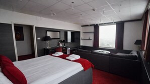 Een moderne hotelkamer met een groot bed, een bank, een bureau en een groot raam.