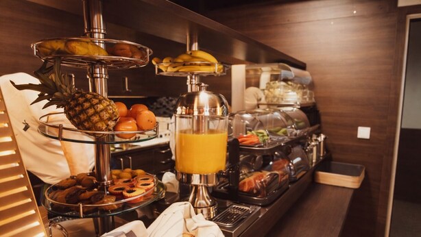 Een buffet met diverse gerechten, waaronder fruit, gebak en een sapautomaat.