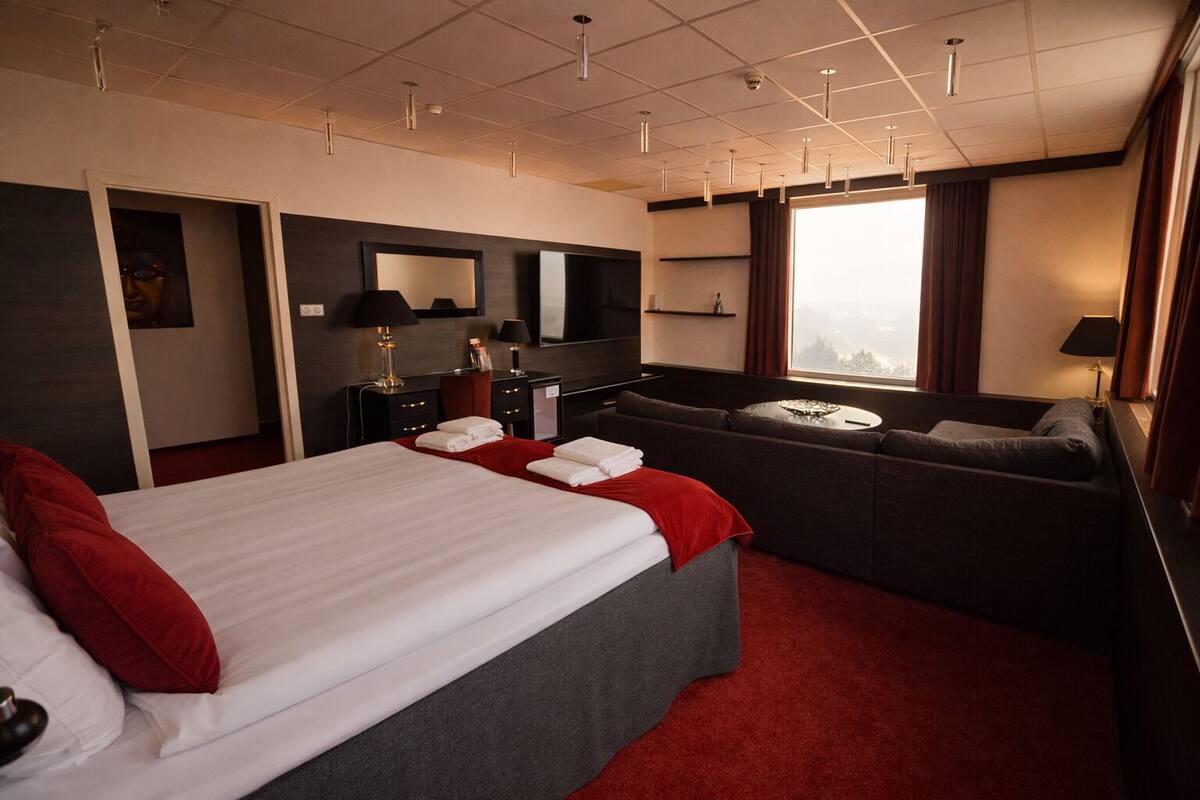 Une chambre d’hôtel avec un grand lit, un canapé, un bureau et une grande fenêtre avec des rideaux.
