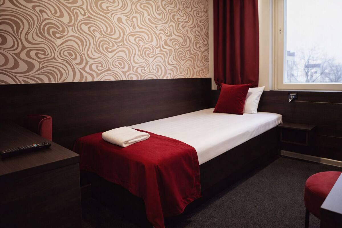 Une chambre d’hôtel avec un lit simple, un bureau, une chaise et une fenêtre avec des rideaux.