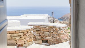 On aperçoit, à travers une porte ouverte, un chemin de pierre menant à un bâtiment blanc doté d’un mur de pierre, qui surplombe un paysage côtier.