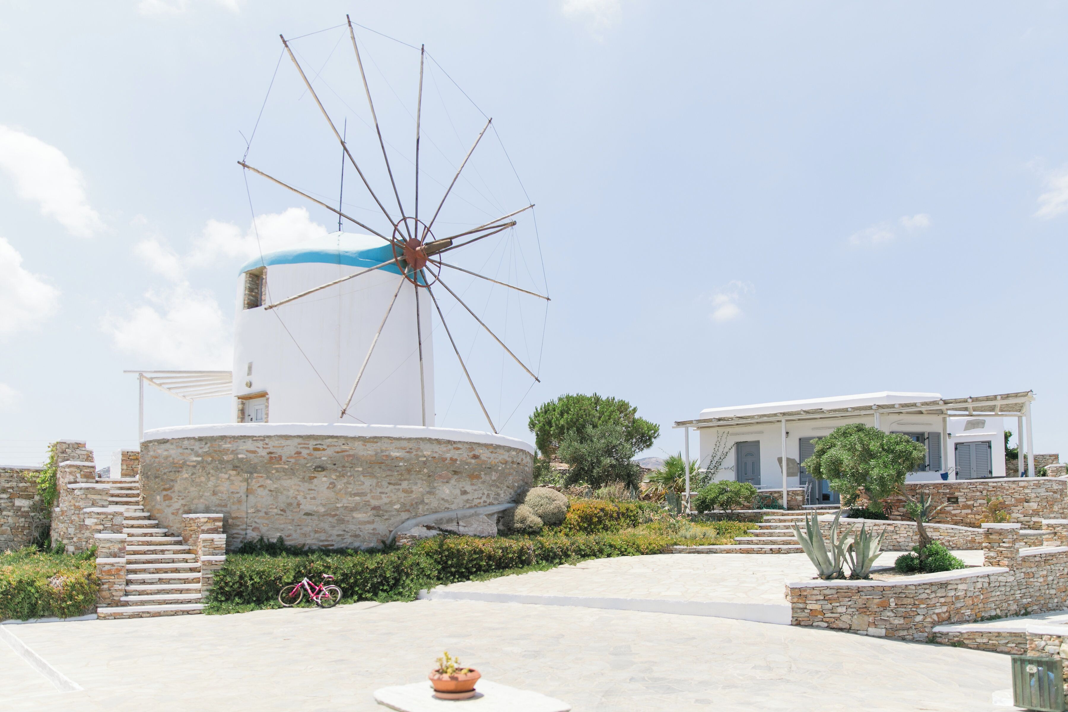 Un molino, una escalera de piedra y un edificio con fachada blanca y contraventanas azules.