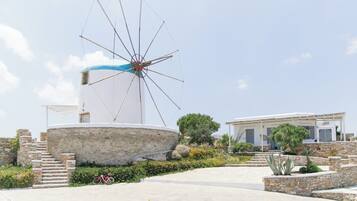 Un molino, una escalera de piedra y un edificio con fachada blanca y contraventanas azules.