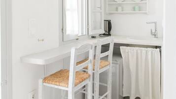 Une cuisine blanche avec une fenêtre, un évier et une étagère où sont rangées des assiettes.