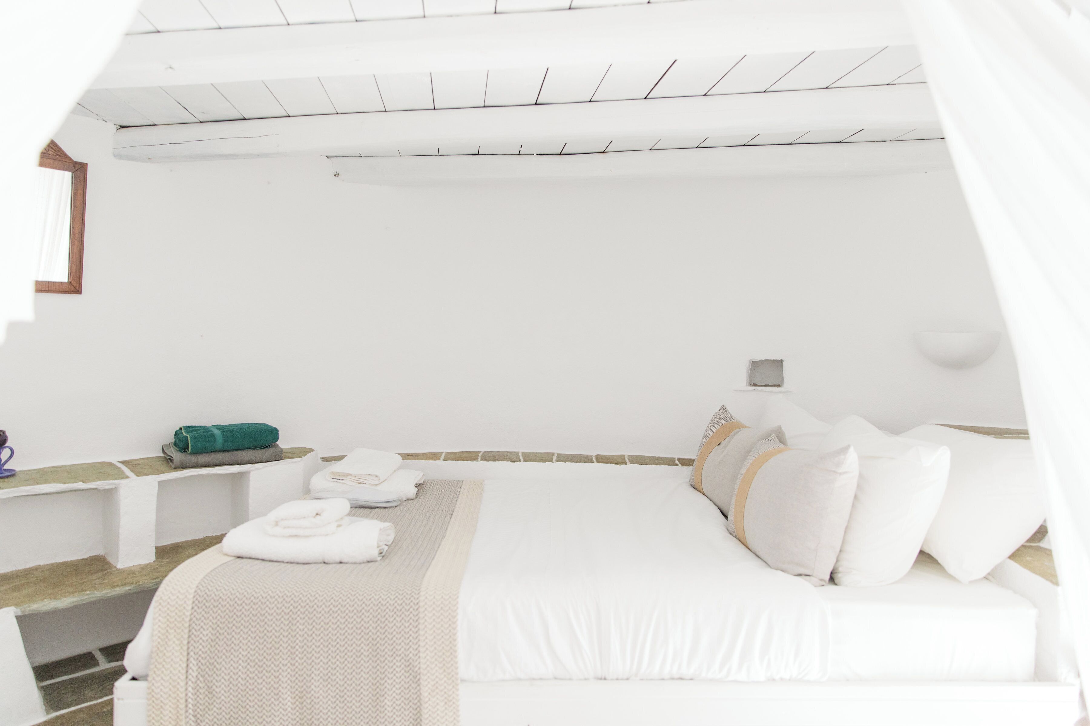 Een witte, minimalistische slaapkamer met een bed, nachtkastjes en een raam.