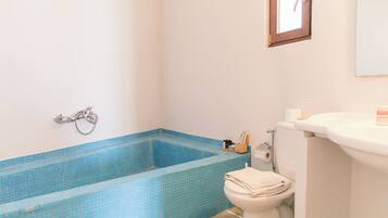 A bathroom with a blue-tiled bathtub, a toilet, and a sink.