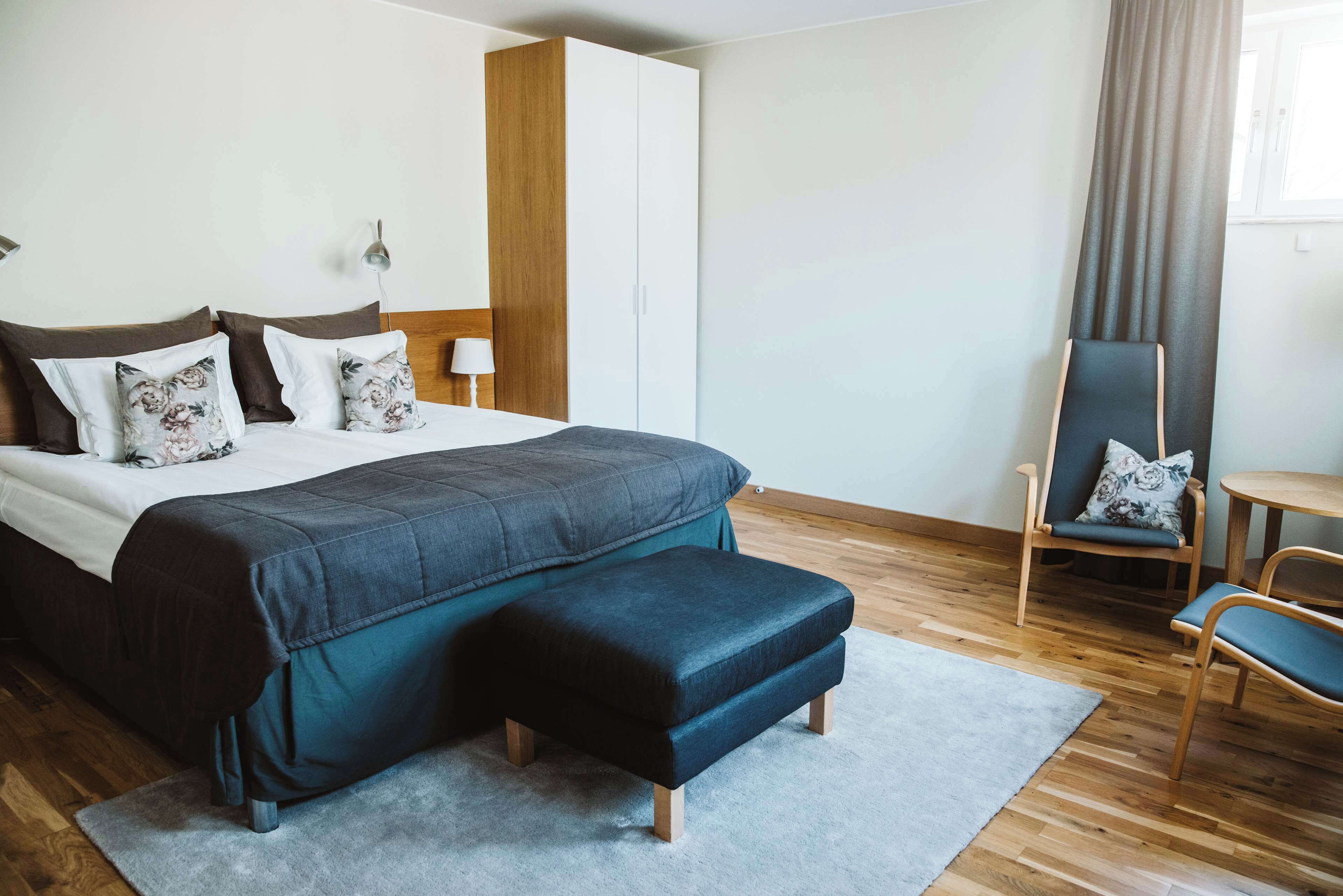 A modern hotel room with a large bed, a wooden wardrobe, a desk, and a chair.