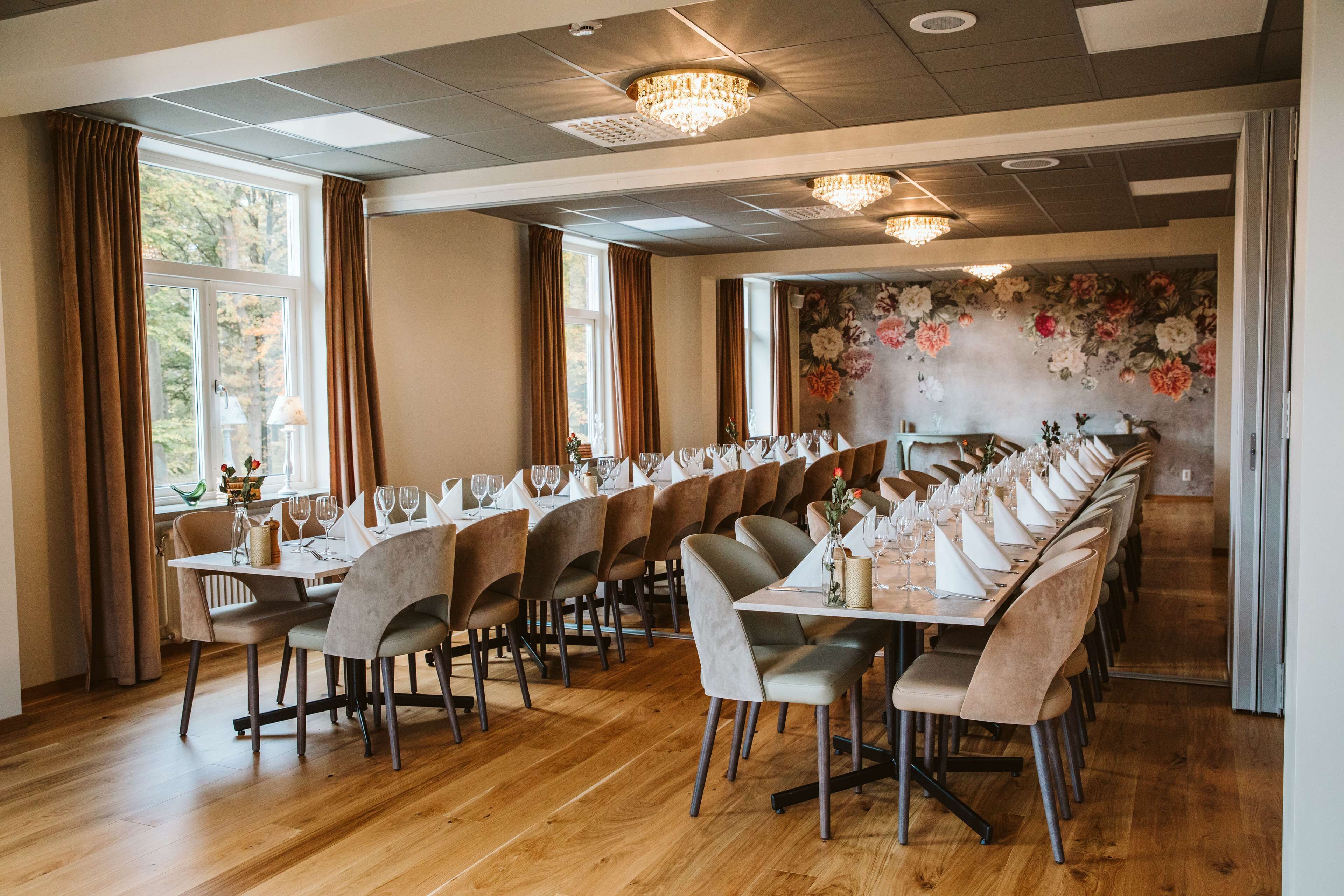 A long dining table set with chairs, a chandelier, and a floral wall mural.