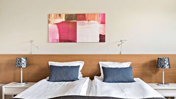 A neatly made bed with white and dark bedding, two blue pillows, and a wooden headboard. There are two bedside tables with lamps and a painting above the bed.