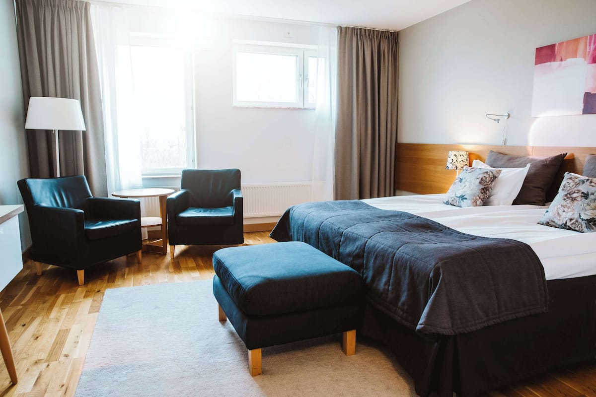 Una habitación de hotel con una cama, dos sillas, una mesita y una lámpara.