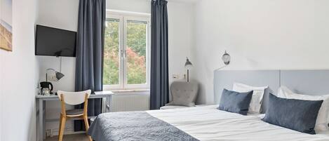 A bedroom with a bed, a desk, a chair, a TV, and a window with curtains.