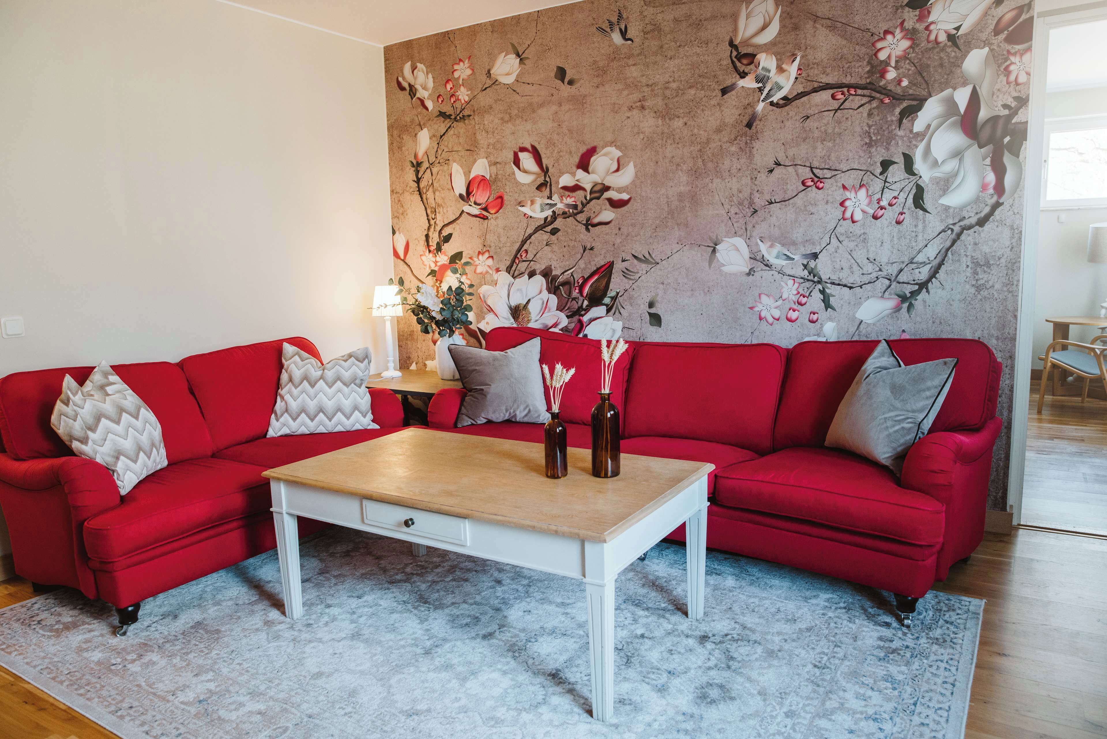 Una sala de estar con un sofá rojo, una mesa de centro blanca y un mural floral en la pared.