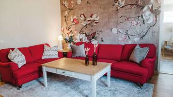 A living room with a red sofa, a white coffee table, and a floral mural on the wall.