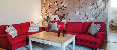 Una sala de estar con un sofá rojo, una mesa de centro blanca y un mural floral en la pared.