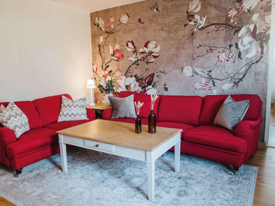 A living room with a red sofa, a white coffee table, and a floral mural on the wall.