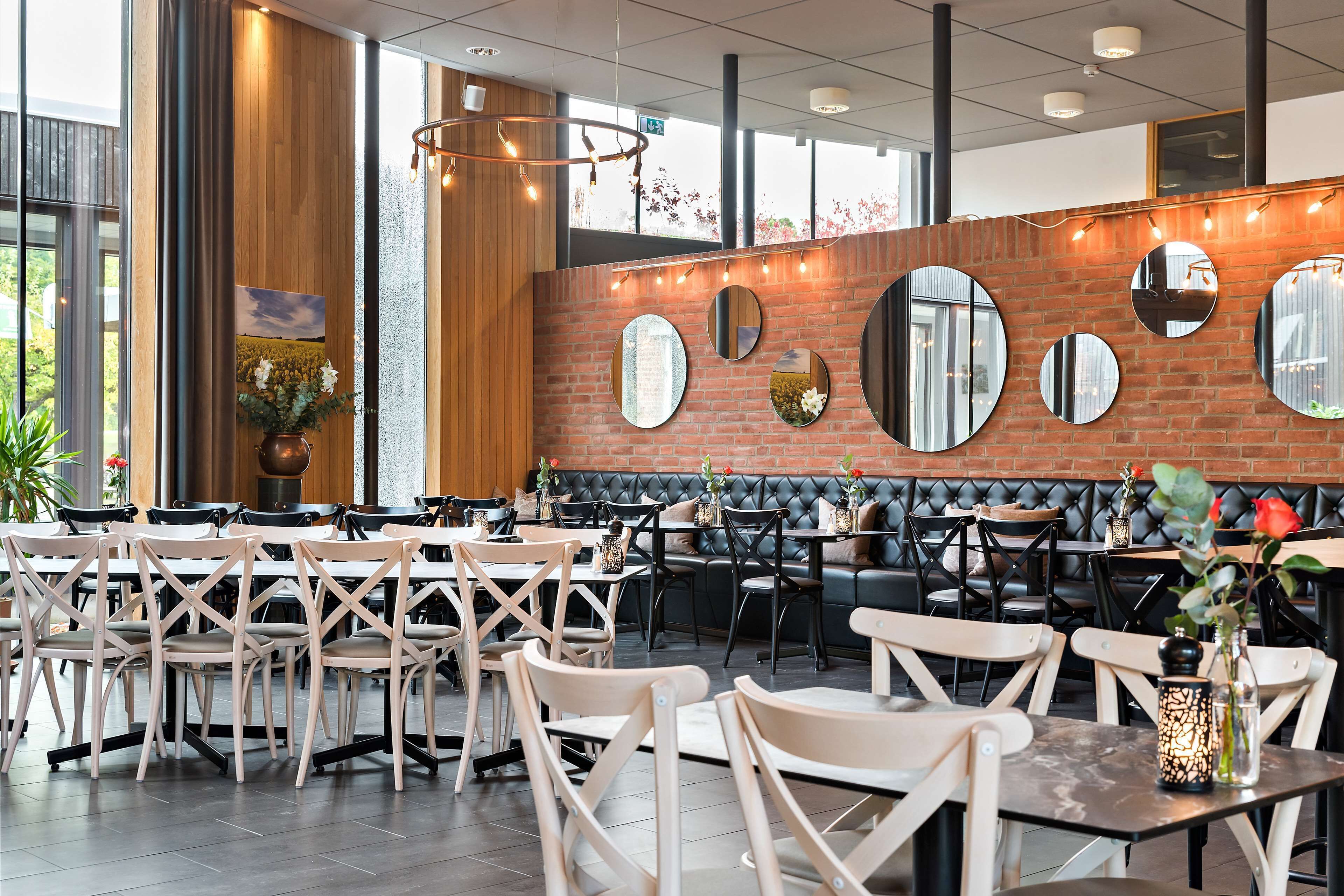 Een restaurant met een bakstenen muur, ronde spiegels en een mix van houten en gestoffeerde zitplaatsen.