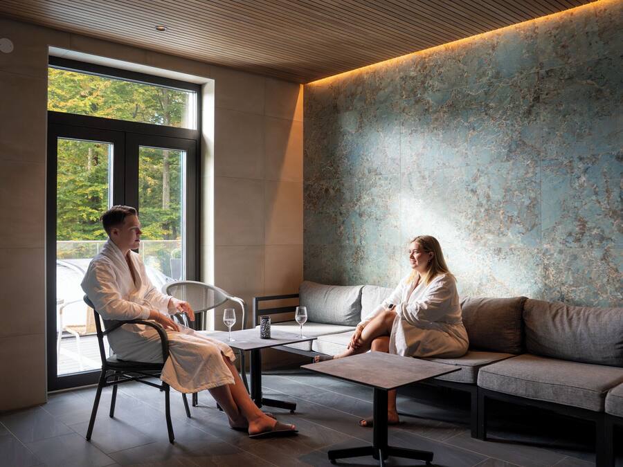 A modern interior with a glass door leading to an outdoor area, a sofa, a table, and two people in robes.