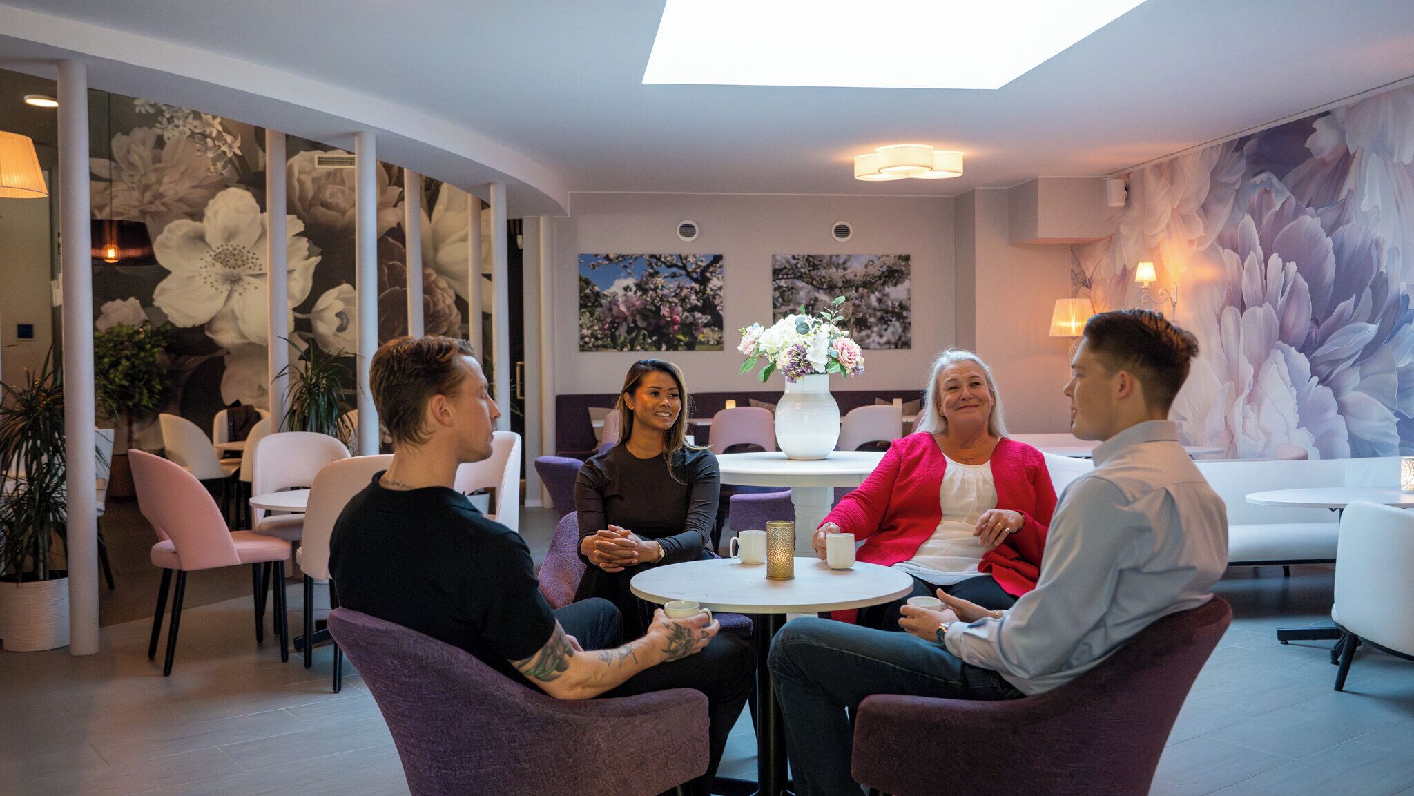 A modern interior with round tables and purple chairs, floral wall art, and a skylight.