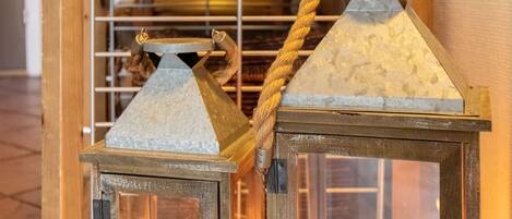 Deux lanternes rustiques dotées d’anses en corde, une bougie à l’intérieur, et une étagère en bois sur laquelle sont disposés divers objets en arrière-plan.