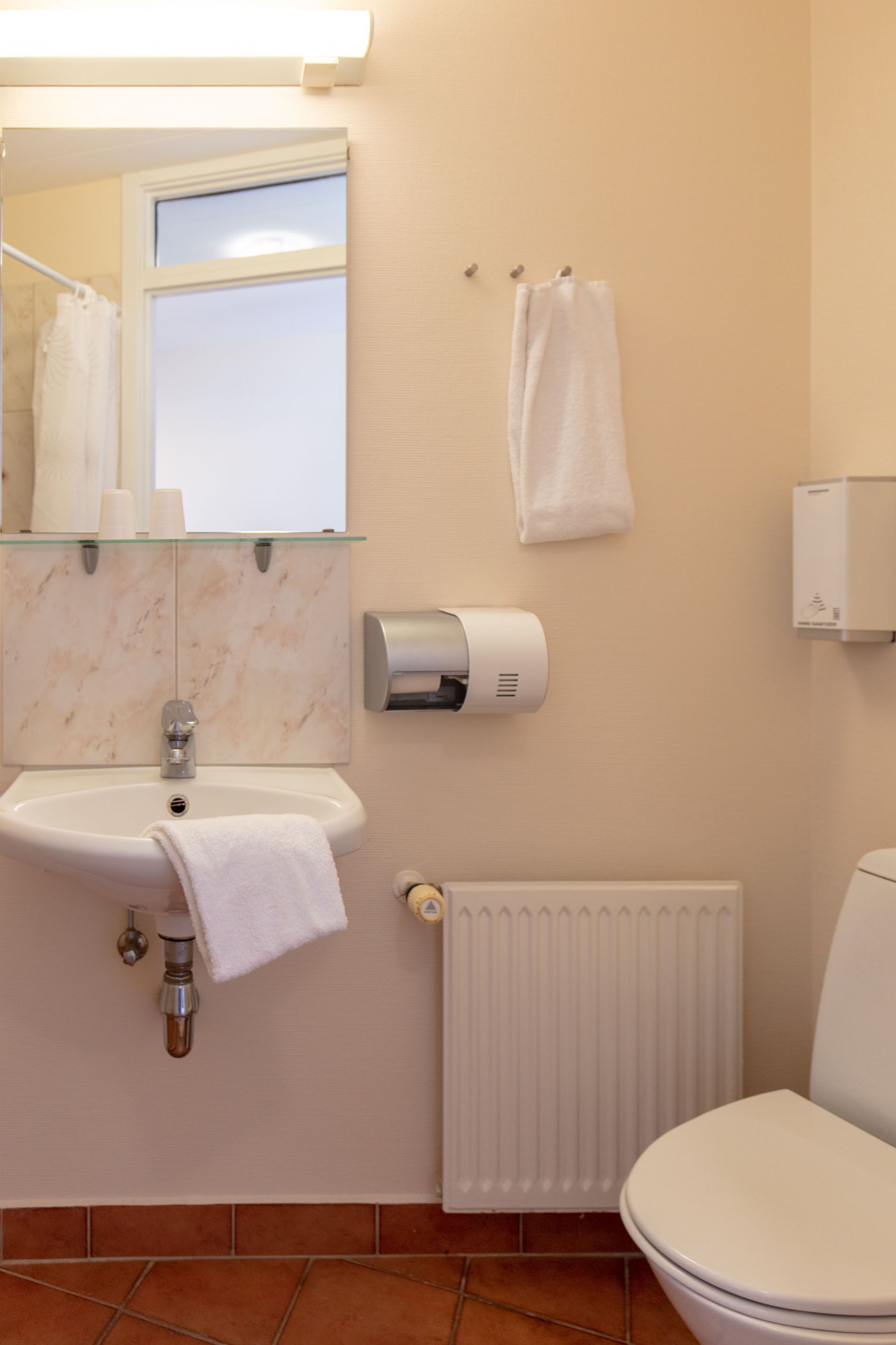 A bathroom with a sink, mirror, towel rack, toilet, and radiator.
