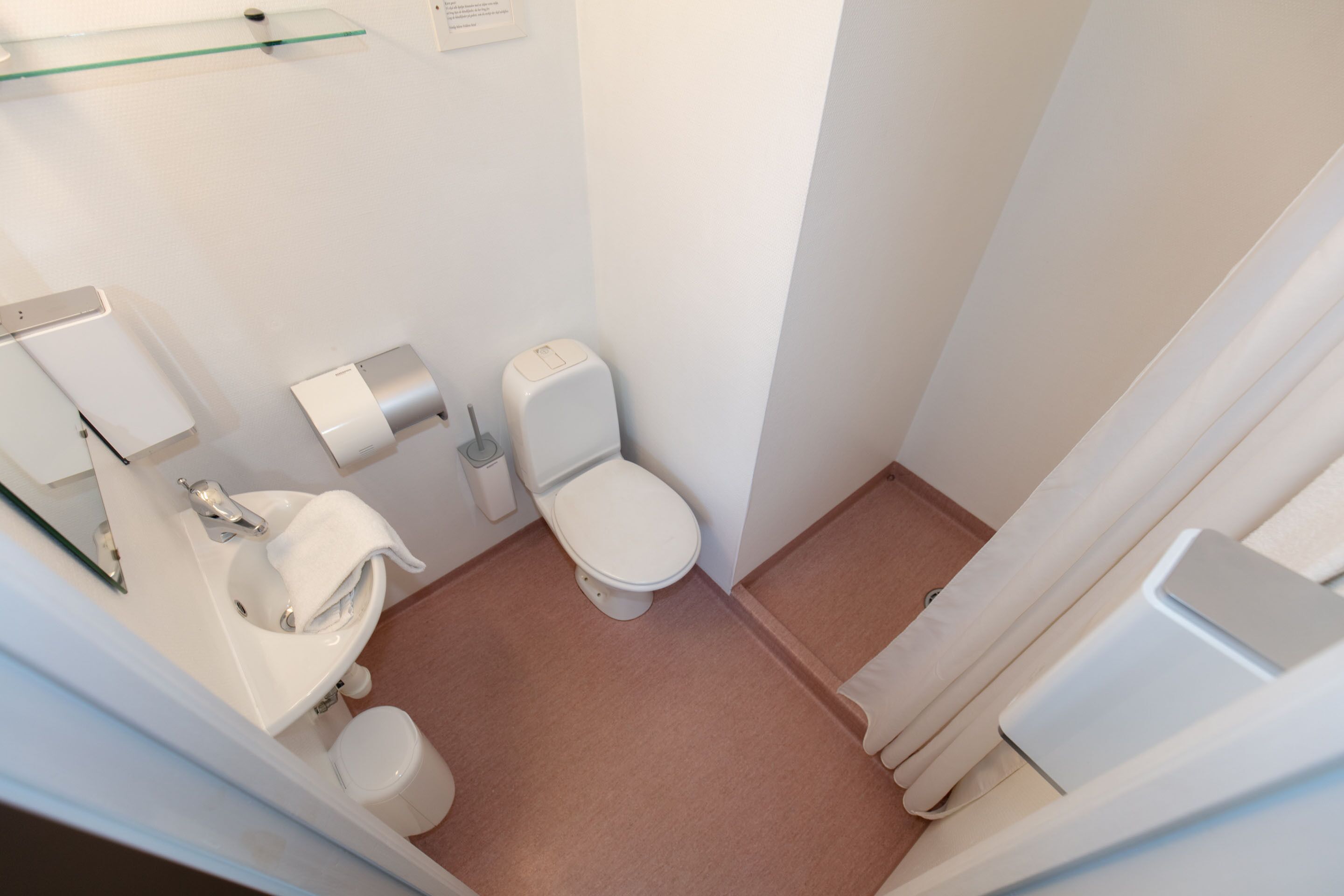 Pieni, moderni kylpyhuone, jossa on wc, pesuallas ja lasihylly.