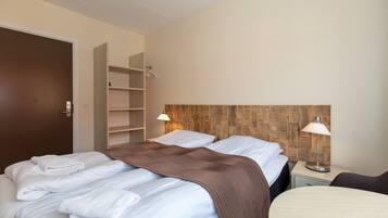 Una habitación de hotel con dos camas, un cabecero de madera, lámparas de noche, una mesita y un armario.