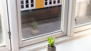 Una ventana con vistas a un edificio amarillo con marcos de ventana blancos y una pequeña planta en maceta en el alféizar.