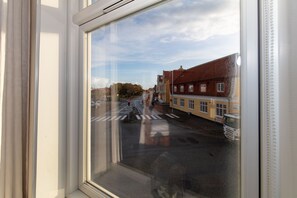 Blick durch ein Fenster auf eine Straße mit Gebäuden, einer Fußgängerüberweg und einer Ampel.