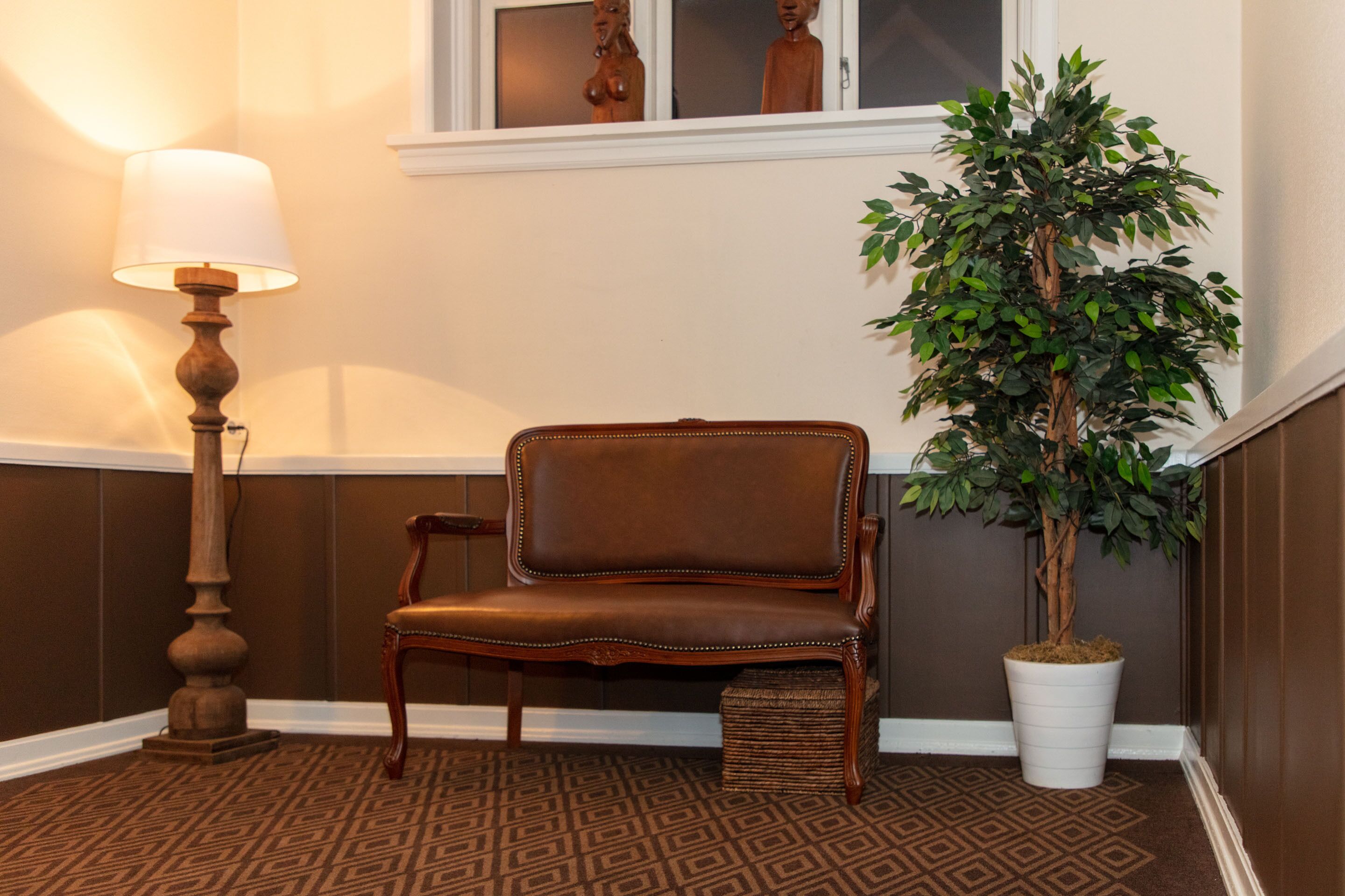 Eine Ecke mit einem braunen Teppich mit Muster, einem braunen Ledersessel, einem weißen Blumentopf und einer Stehlampe.
