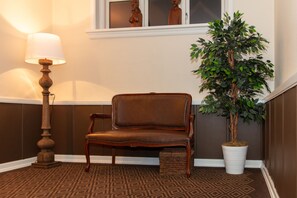 Eine Ecke mit einem braunen Teppich mit Muster, einem braunen Ledersessel, einem weißen Blumentopf und einer Stehlampe.