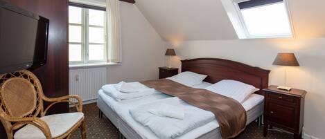 A neatly arranged bedroom with a bed, bedside tables, a television, and a window.
