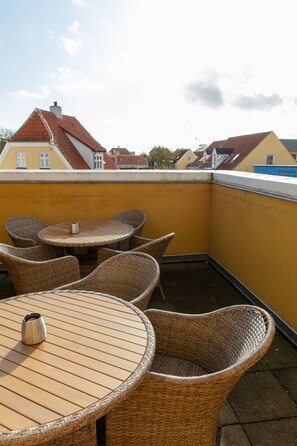 Eine Dachterrasse mit Korbmöbeln und einem Tisch, mit Blick auf eine Häuserreihe.