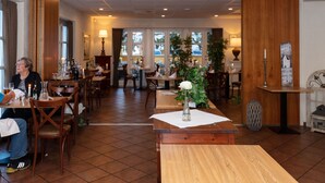 Un restaurante con mesas y sillas de madera, un jarrón con flores y vista a coches estacionados a través de las ventanas.