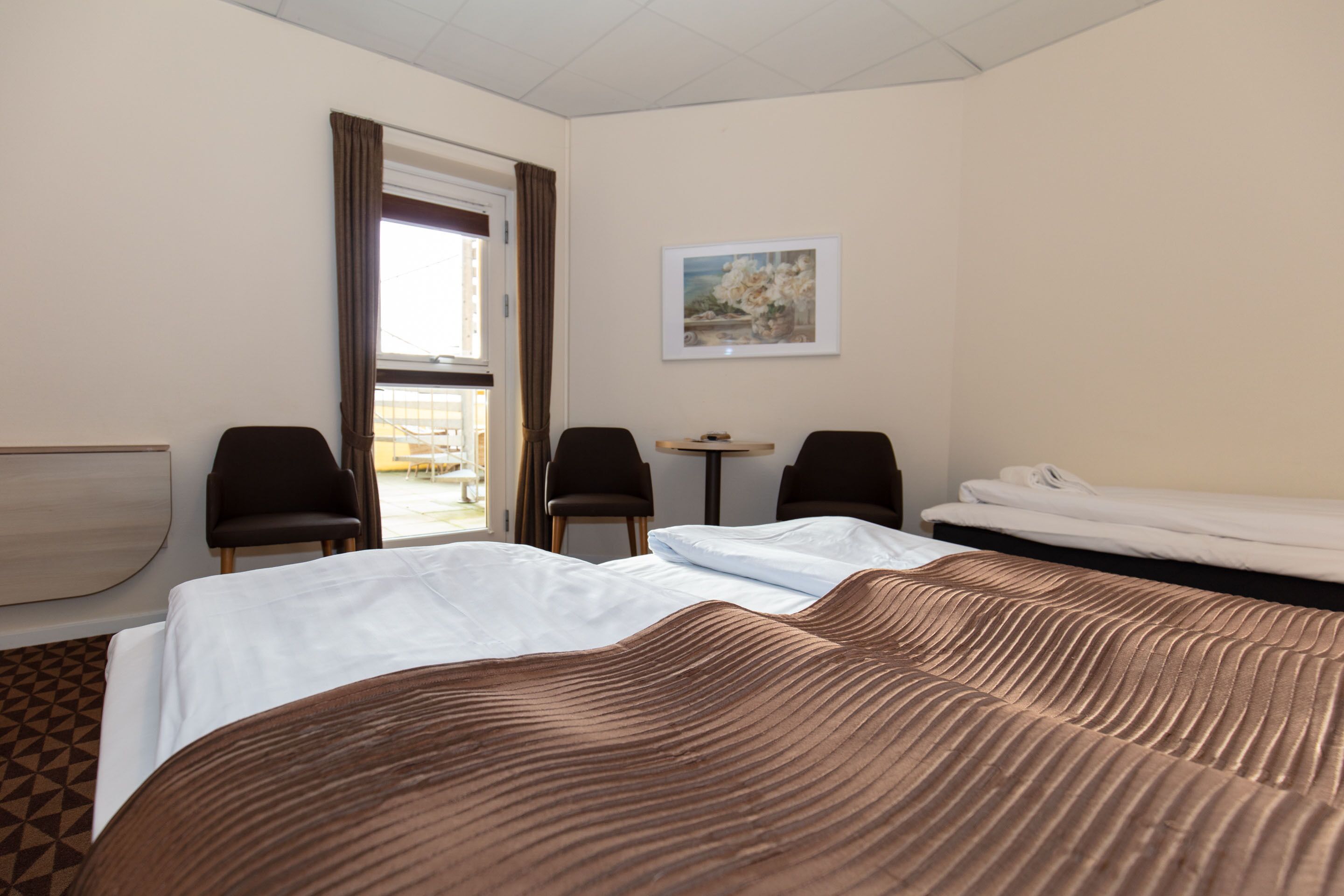 A hotel room with a large bed, two chairs, a small table, and a painting on the wall.