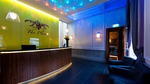 A reception area with a wooden reception desk, a wall-mounted sign reading "The Place," and a seating area with blue chairs. - The Place (Edinburgh)