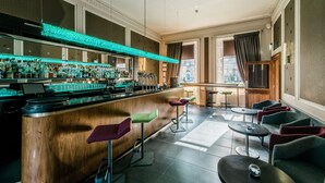 A bar area with a wooden counter, bar stools, and a variety of bottles. There are tables and chairs for seating. - The Place (Edinburgh)