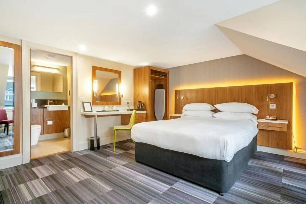 A modern hotel room with a large bed, a desk, and a bathroom.