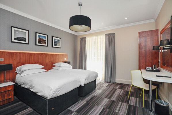 A hotel room with a large bed, a desk, a chair, and a mirror. There are three framed pictures on the wall and a window with curtains. - The Place (Edinburgh)