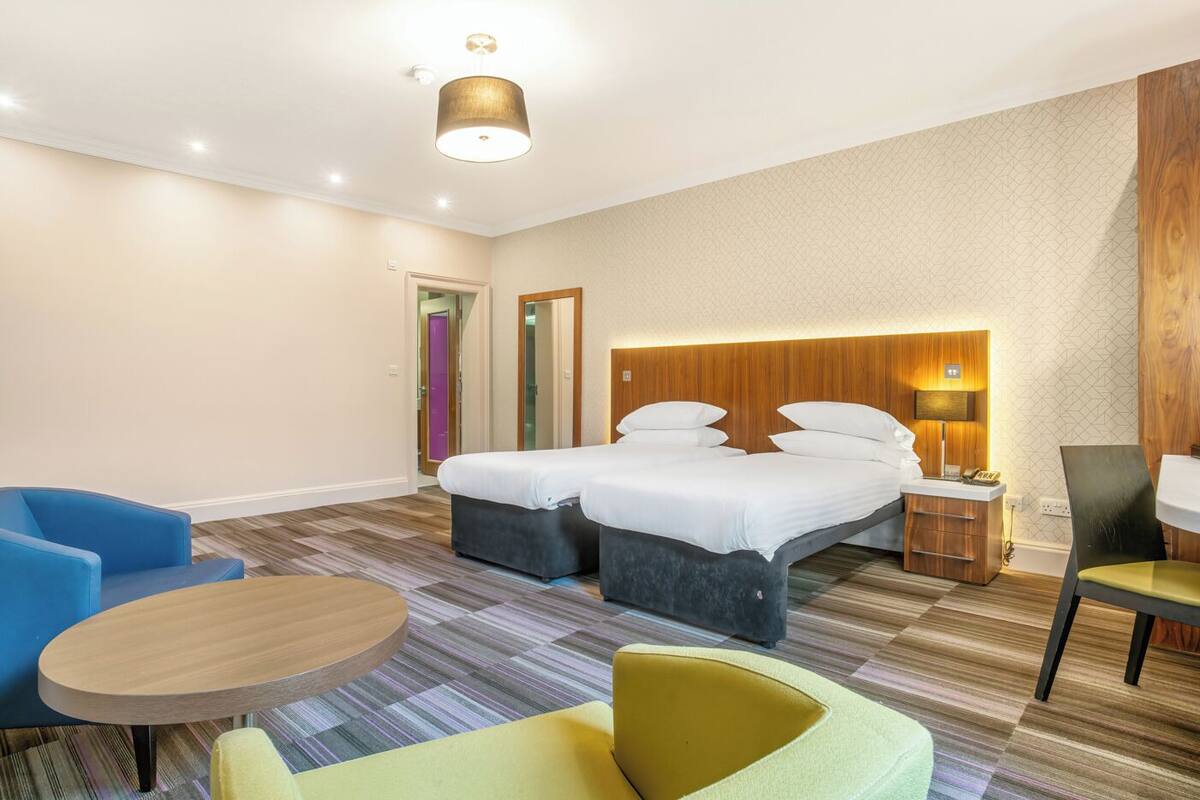 A hotel room with a large bed, two bedside tables, a desk, a chair, and a sofa.