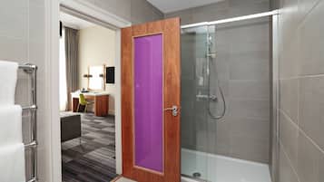 A modern bathroom with a glass shower enclosure, a wooden door with a purple panel, and a visible bathroom counter with a chair.
