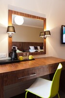 Une chambre d’hôtel avec un bureau en bois, un miroir, deux lampes, une chaise et un lit avec une tête de lit.