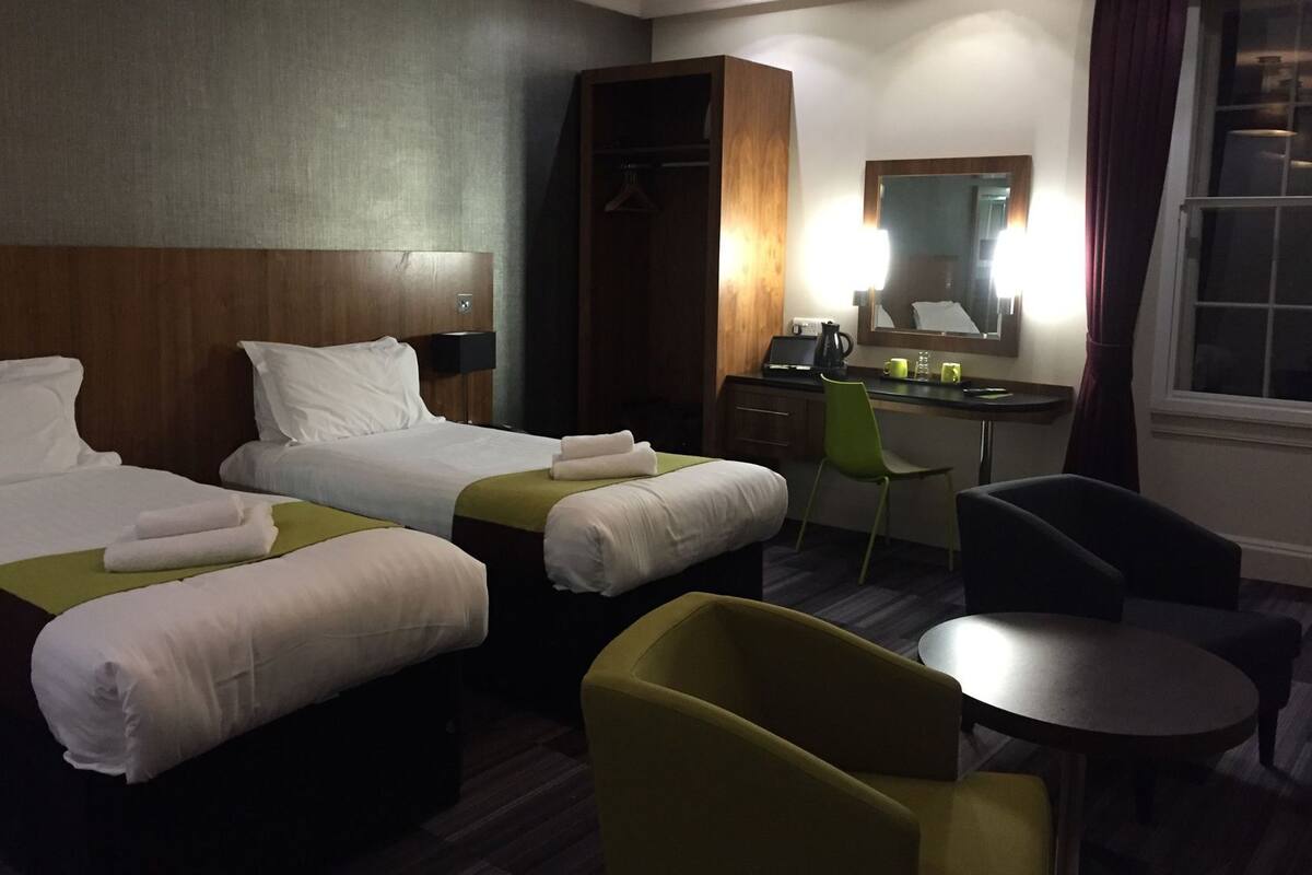 A hotel room with two beds, a desk, a chair, a round table, and a mirror.