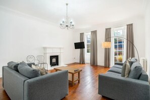 A modern living room with two grey sofas, a fireplace, a flat-screen TV, and a chandelier. - The Place (Edinburgh)