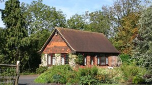 A traditional brick house with a sloped roof, surrounded by lush greenery and a paved driveway. - Tovey Lodge (Hassocks)