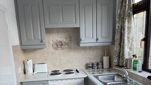A compact kitchen with grey cabinets, a built-in oven, a stovetop, and a stainless steel sink. - Tovey Lodge (Hassocks)