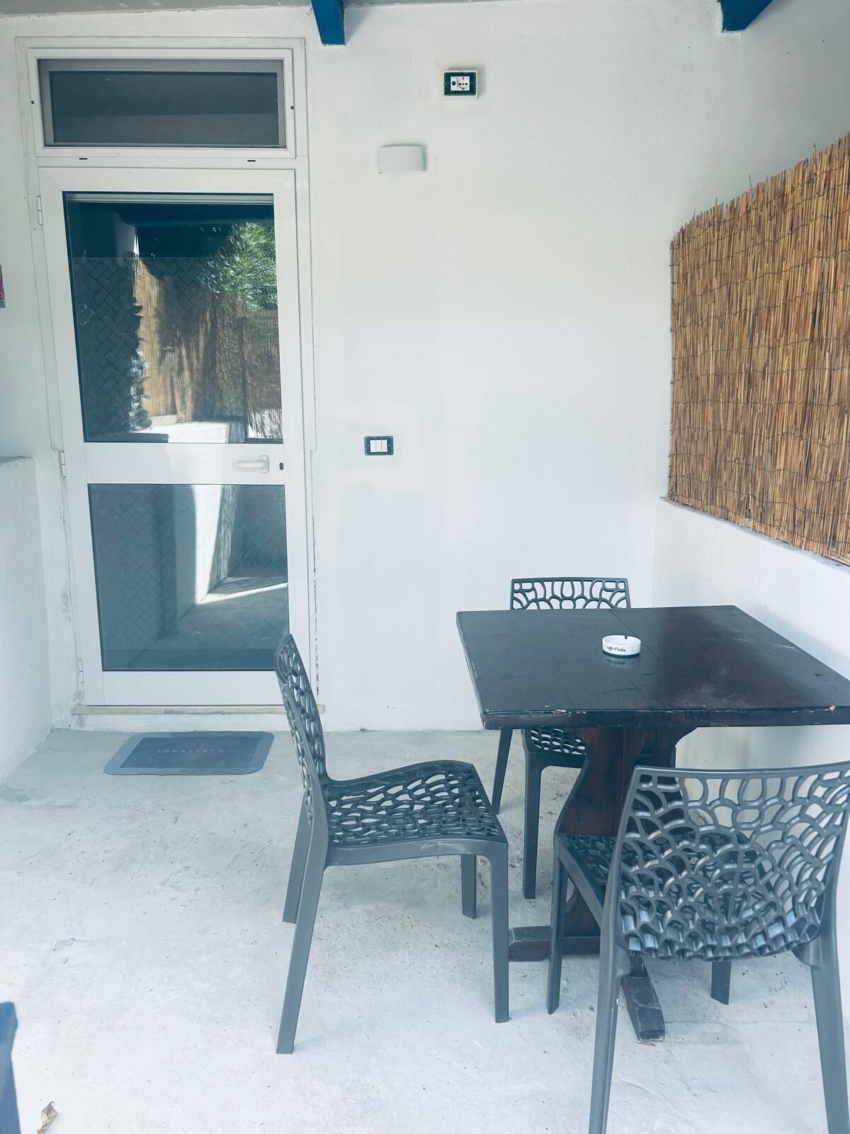 Un'area patio con tavolo e sedie, una porta scorrevole in vetro e una presa elettrica a parete.