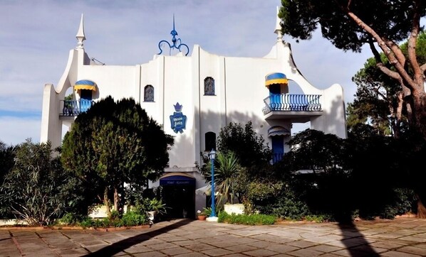 A white building with blue accents, a sign reading "Meson Sells," and a balcony with blue railings.