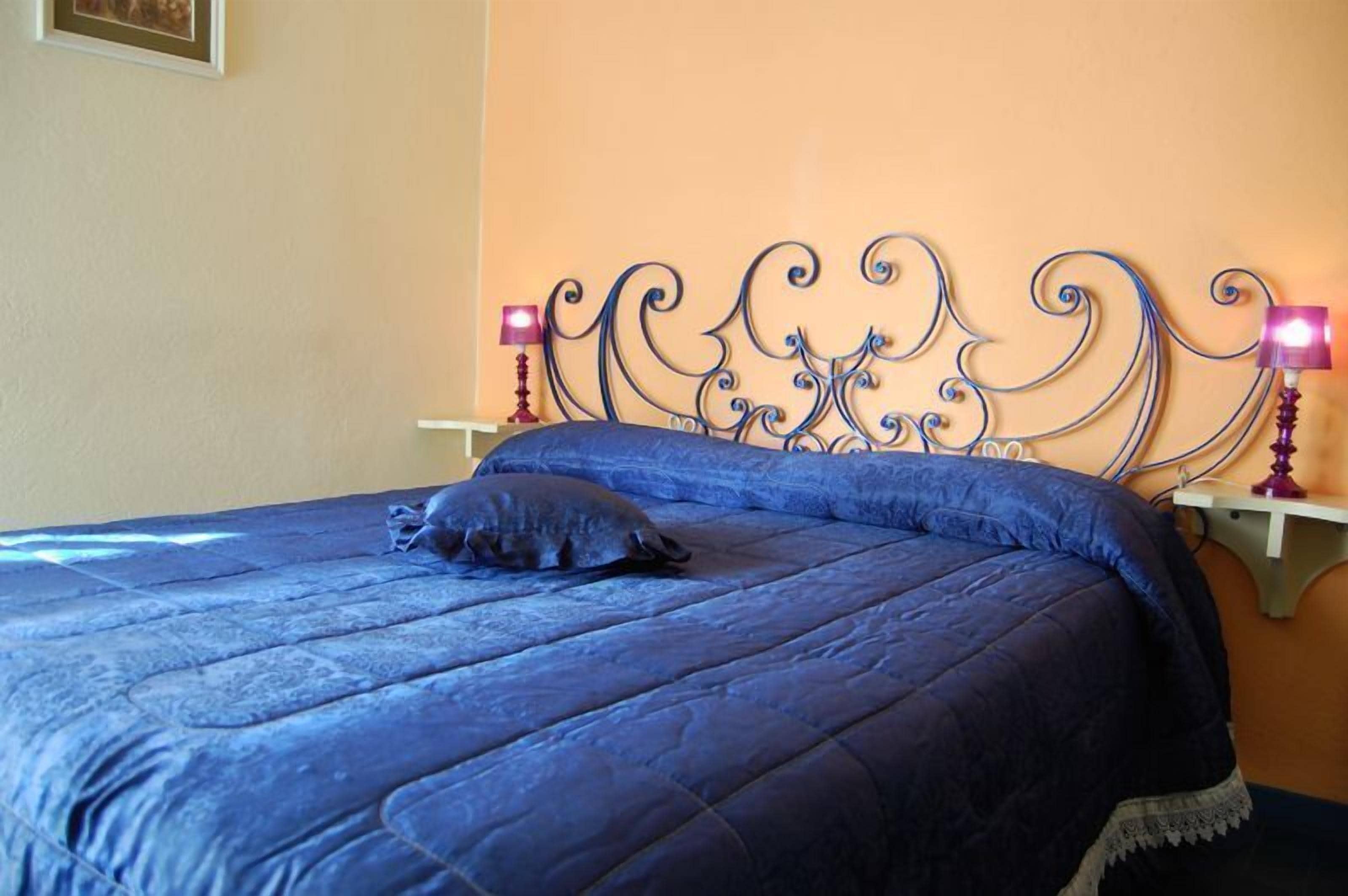A bed with a blue quilt and a decorative metal headboard. There are two bedside lamps on either side of the bed.